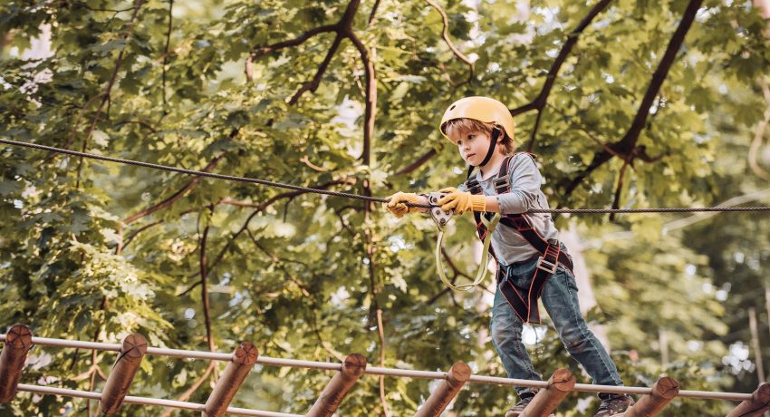 Balance beam and rope bridges. Go Ape Adventure. Child concept. Climber child on training. Portrait of a beautiful kid on a rope park among trees. Carefree childhood.