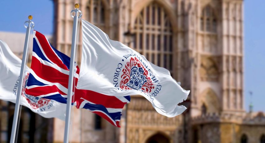 London, UK, April 2023: Flags with the emblem of the coronation of King Charles III and of UK waving with Westminster Abbey in the background. Illustrative editorial 3d illustration render.